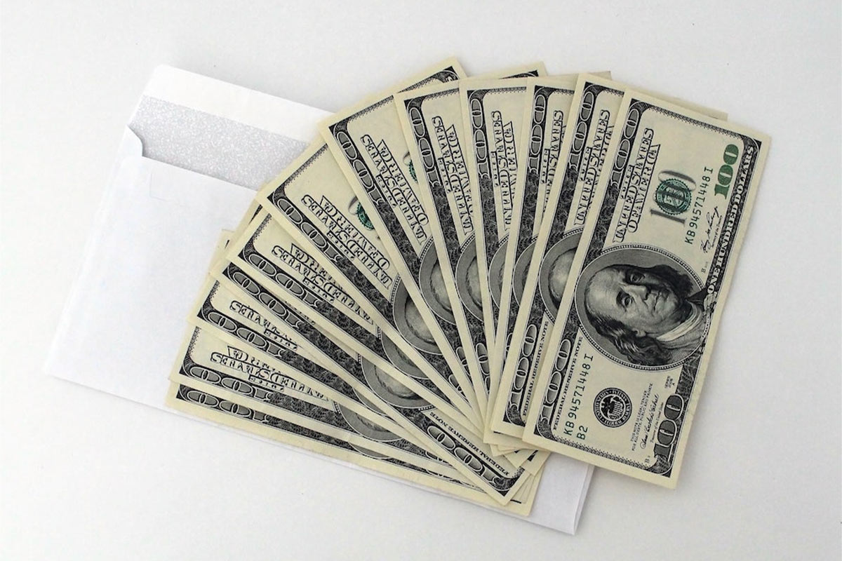 Mehrere 100-Dollar-Scheine fächerförmig auf einem weißen Umschlag ausgelegt.