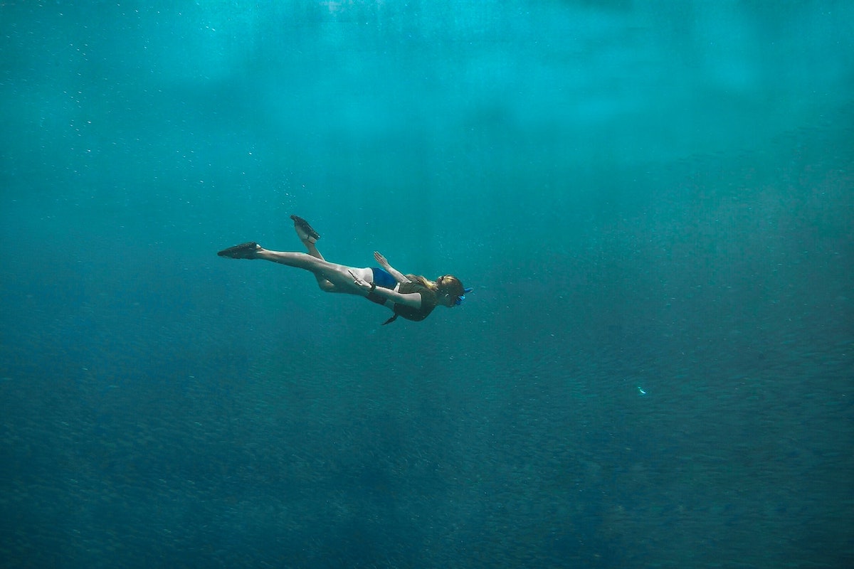Frau mit Schnorchel schwimmt unter Wasser im offenen Meer.