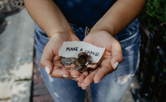 Person hält Kleingeld und ein Papier mit Aufschrift "Make a change" in der Hand.